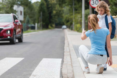 Young mother squats on the sidewalk and explains to the little boy how to cross the street safelyの写真素材