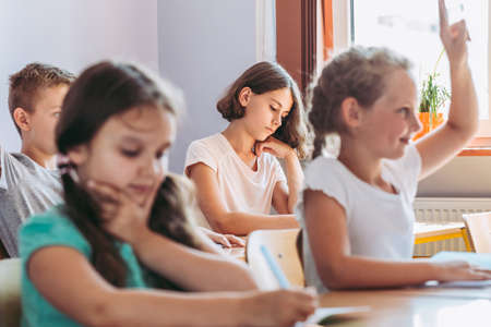 Smart smiling girl raising her hand to answer the question during classes