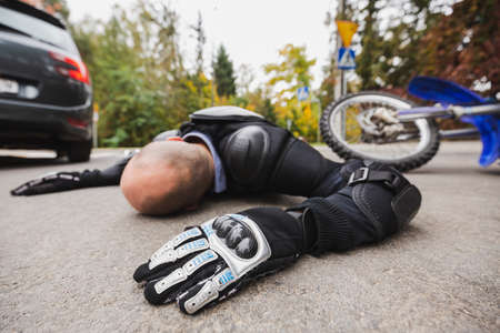 Motorcycle driver without the helmet laying on the roadの写真素材