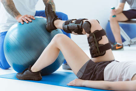 Pretty patient sitting on the blue mat in the gym and training with the ballの写真素材
