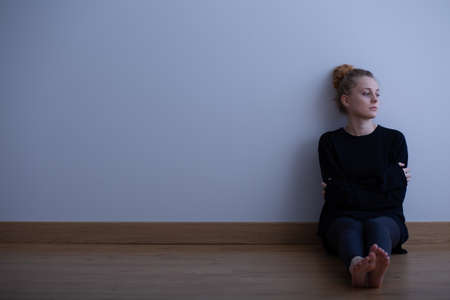 Picture of a sad teenage girl suffering from loneliness, sitting alone on the floor, copy space on empty wallの写真素材