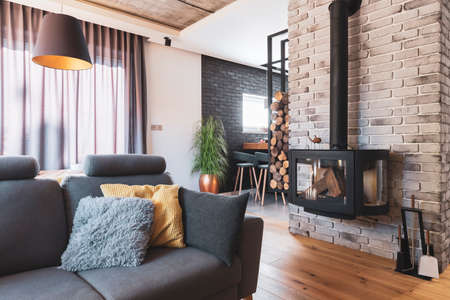 Grey couch with pillows next to modern fireplace in stylish living room interior