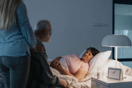 Older man staying awake by his sick wife in the hospital bedの写真素材