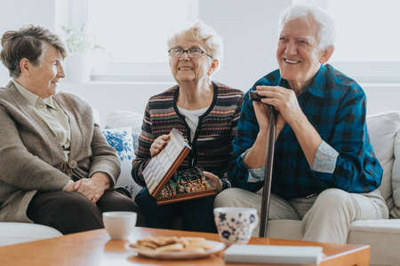 Senior friends sit on the sofa in the living room and play chess in a nursing homeの写真素材