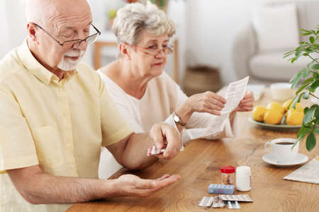 Senior couple sitting at dining table taking medicinesの写真素材