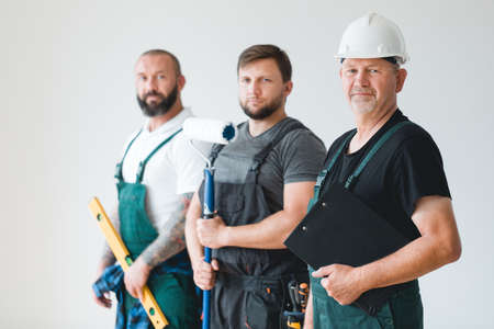 Crew of three professional builder wearing overalls standing in empty interiorの写真素材