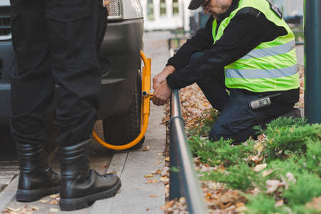 Close-up of policeman setting a wheel clamp on a car parked by the pavementの写真素材