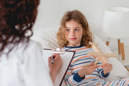 Little patient playing with wooden model and talking to the nurseの写真素材