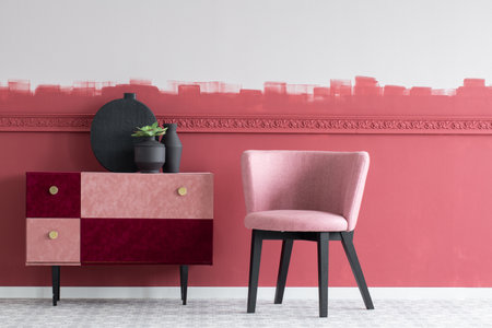 Stylish small pastel pink chair next to trendy pink and burgundy commodeの写真素材