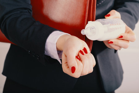Elegant woman, holding a leather briefcase under her arm, checks the temperature of milk in a baby bottleの写真素材