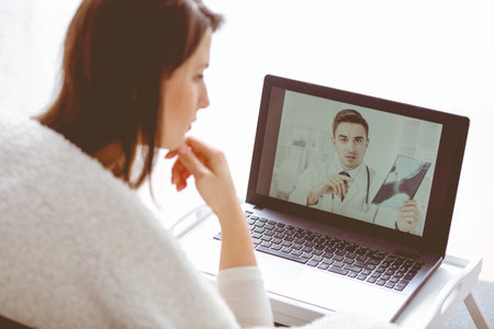 Handsome doctor explaining medical exam results to his patient over the internet conversationの写真素材