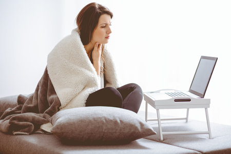 Sick woman with flue sitting at home consulting her doctor via internet conversationの写真素材