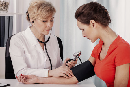 Senior doctor measuring blood pressure of young female patient in medical clinic