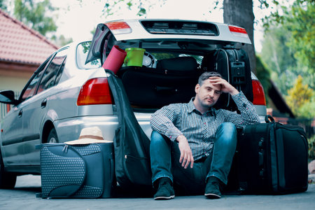 Handsome man sitting on the road next to car with open trunkの写真素材