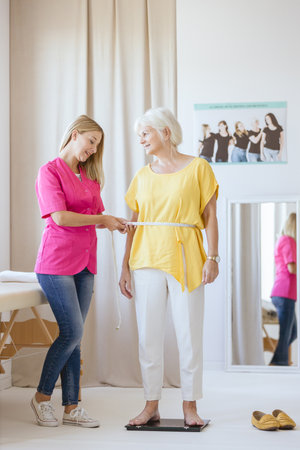 Young dietician measuring her middle-aged patient waist on a control meetingの写真素材