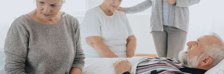 Three women from family staying awake by dying senior grandfatherの写真素材