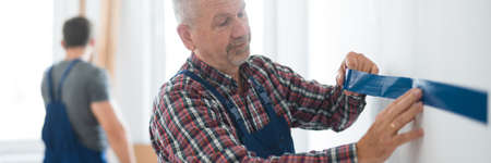 Professional builder puts a tape on an empty wall before painting itの写真素材