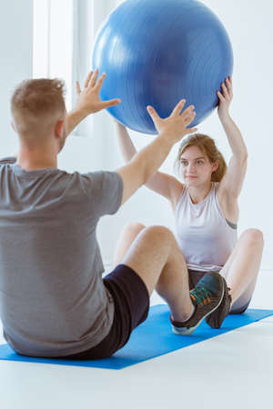 Pretty patient sitting on the blue mat in the gym and training with the ballの写真素材