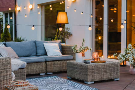 Summer evening on the terrace of beautiful suburban house with patio with wicker furniture and lightsの写真素材