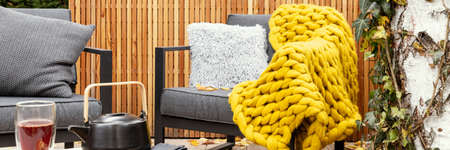 Cozy garden with gray armchairs, yellow blanket and kettle and glass on the tableの写真素材