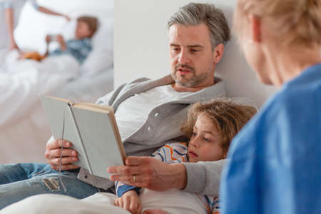 Caring father reading a book to his sick daughterの写真素材