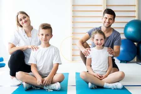 Kids sitting on blue yoga mats with their professional physicianの写真素材