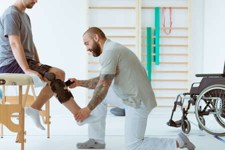 Helpful professional physiotherapist helps the patient to put on an orthosis for the first timeの写真素材
