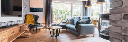Elegant living room with light wooden floor, gray couch and wing back chair and big tv on the wallの写真素材