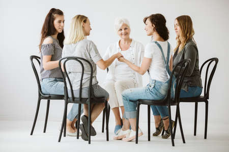 Women holding hands and sitting in circle during support group for females with problemsの写真素材
