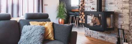Gray couch with pillows next to modern fireplace in stylish living room interiorの写真素材