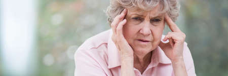 Senior woman holding her head because of migraine, copy space on the photoの写真素材