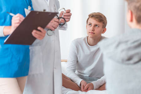 Teenage young patient is sitting cross-legged on a hospital bed during hospitalizationの写真素材