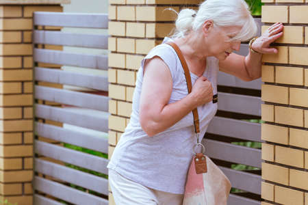 Senior woman is holding her chest while standing on the street, heart attack conceptの写真素材