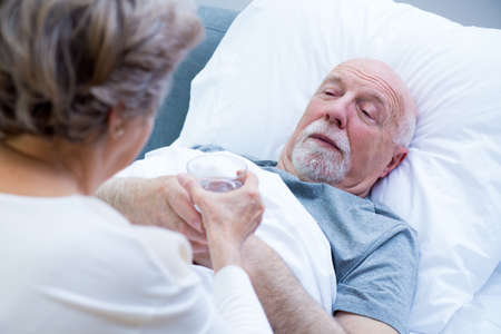 Helpful senior wife giving glass of water to her sick husbandの写真素材