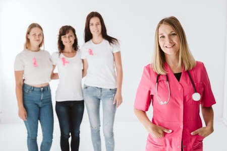 Young female doctor wearing pink uniform standing in front of patients wearing white t shirts and pink bowsの写真素材