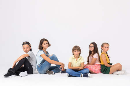 Group of young happy kids sitting in a row in white roomの写真素材