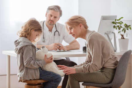 Sad girl with teddy bear and worried grandmother at pediatrician's officeの写真素材