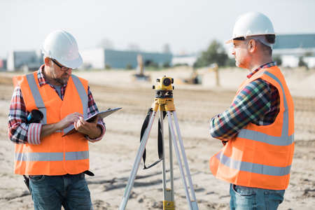 Two builders in uniforms at work using tachometerの写真素材