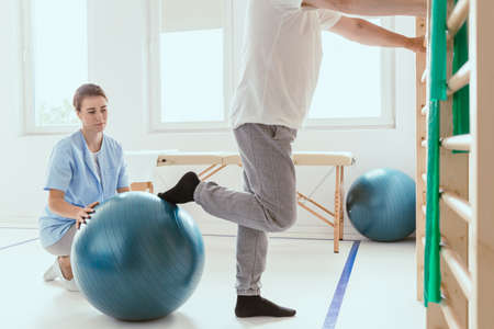Young professional physiotherapist exercising with an injured patient using a blue ballの写真素材