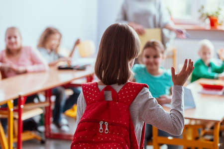 Girl with a red backpack says hello to her friends on her first day of schoolの写真素材