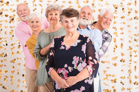 Smiling senior woman wearing elegant blouse standing in front of group of senior happy fiends looking from behind herの写真素材