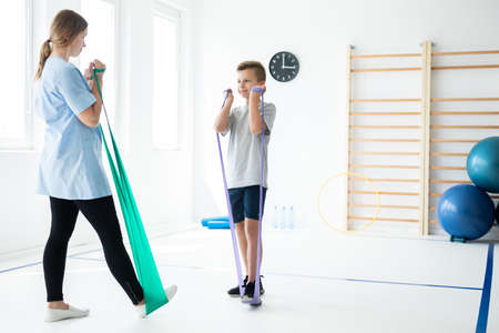 Female physician showing to boy how to perform an exercise with tapesの写真素材