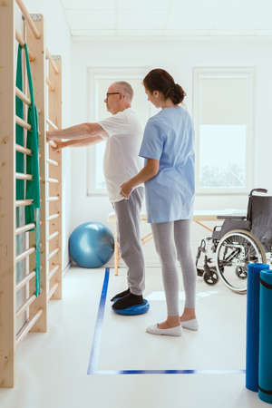 Elderly man doing gymnastic exercises with a young female physiotherapist