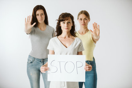 Three young women are standing next to each other, one of them holding a piece of paper with the word stopの写真素材