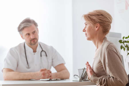 Handsome middle age doctor and female patient at hospital officeの写真素材