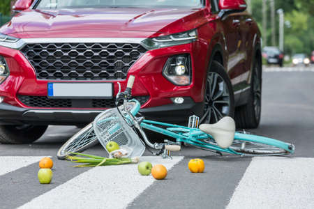 Groceries and a blue bike lies on the street next to the red car that caused the accidentの写真素材