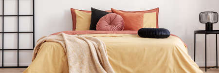 Black round velvet pillow on yellow duvet in trendy bedroom interior with king size bedの写真素材