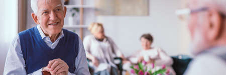 Older man in nursing home talking with a friend in the living roomの写真素材
