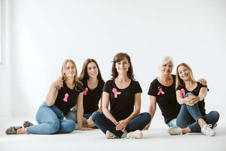 Five women dressed in jeans and black T-shirts with pink bows sitting on the floor of empty interiorの写真素材