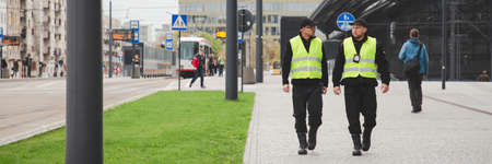 Policemen in reflective vests looking around carefully during patrol in the city centerの写真素材